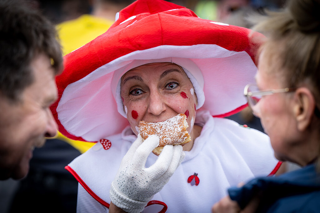 Berlin New Year's Eve Run 2022: Runner in toadstool costume bites into a jelly donut @ SCC EVENTS / Tilo Wiedensohler