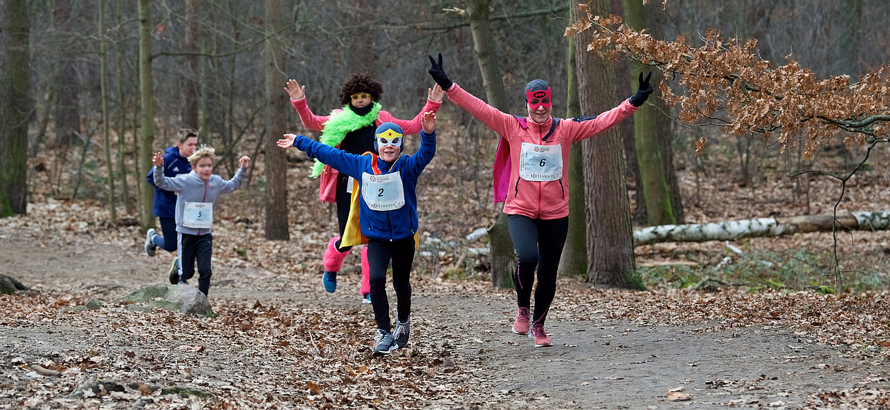 Berlin New Year's Eve run: Costumed family runs joyfully along a forest path with arms raised @ SCC EVENTS / Tilo Wiedensohler
