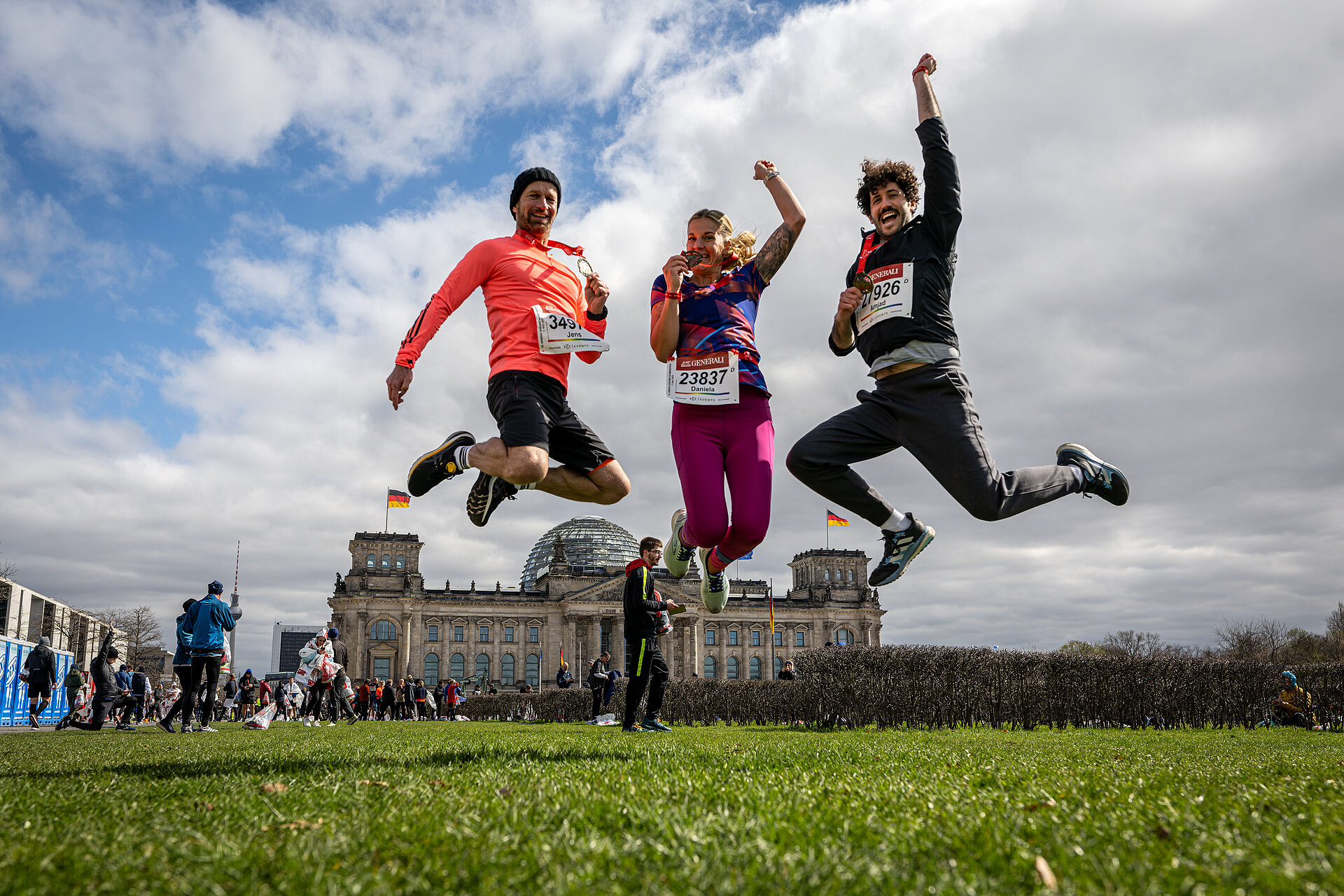 Three finishers jump into the air on the Reichstag lawn.