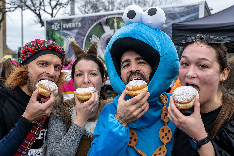 Berliner Silvesterlauf: Kostümierte Läufer:innen 2022 beissen im Ziel  beherzt in Pfannkuchen @ SCC EVENTS / Tilo Wiedensohler