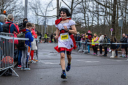 Berliner Silvesterlauf 2022: Kostümierter Läufer passiert Zuschauer in der Zielgasse @ SCC EVENTS / Tilo Wiedensohler