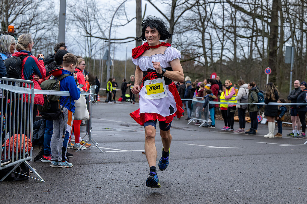 Berliner Silvesterlauf 2022: Kostümierter Läufer passiert Zuschauer in der Zielgasse @ SCC EVENTS / Tilo Wiedensohler