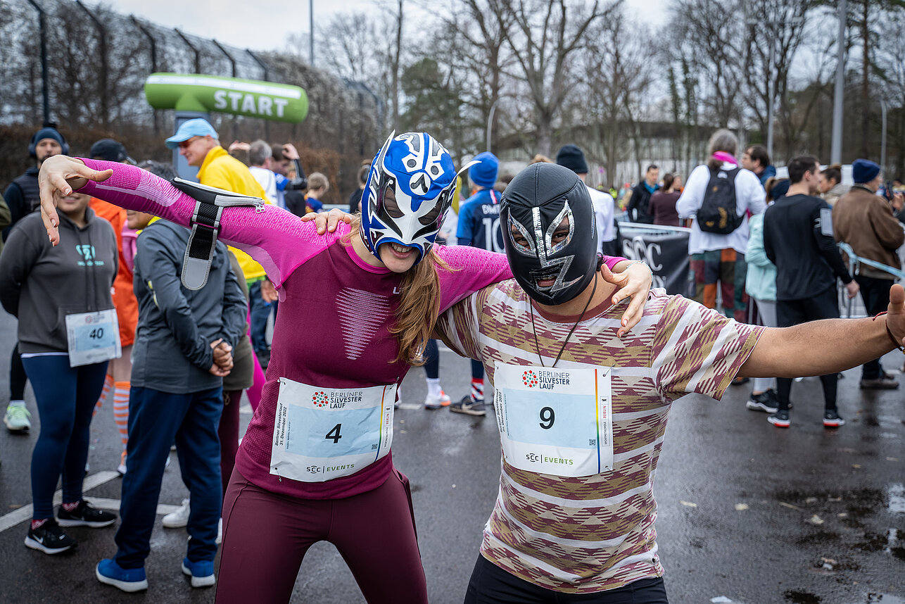 Berlin New Year's Eve run: A pair of runners with wrestling masks smile arm in arm into the camera @ SCC EVENTS / Tilo Wiedensohler